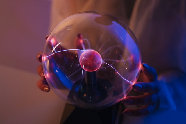 A glass plasma globe with purple and blue light filaments reaching toward a person's hands.