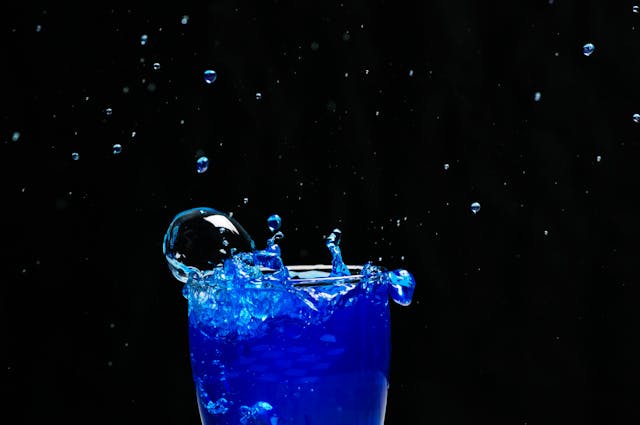 Blue liquid splashing out of a glass against a dark background.
