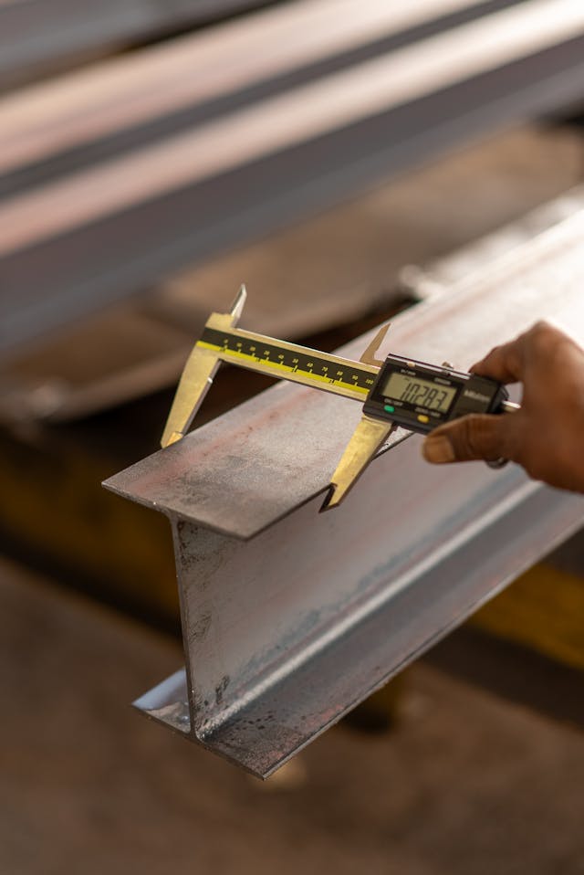 Caliper measuring the width of a steel beam to demonstrate precise length measurement in physics