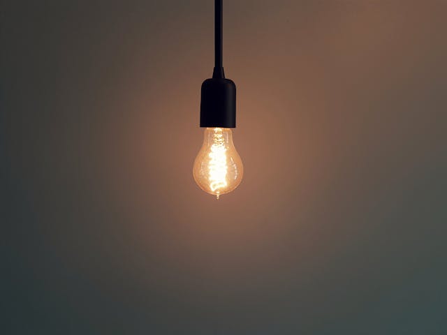 A single vintage light bulb with a glowing filament hanging against a dark background.