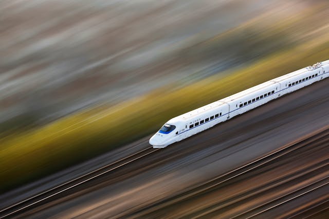 Passenger train moving along straight railroad tracks in an open landscape.