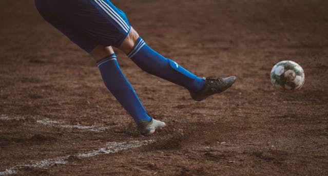 A close-up of a soccer player's legs kicking a ball into the air.