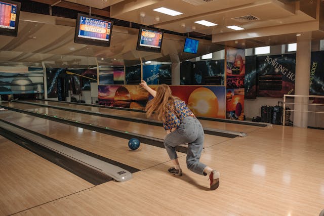 A person throwing a blue bowling ball down a lane toward pins.
